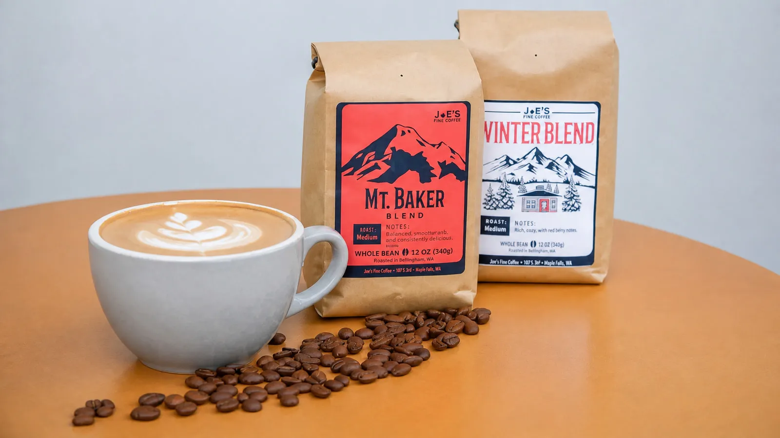 A latte with bags of Joe’s Fine Coffee Mt. Baker Blend and Winter Blend