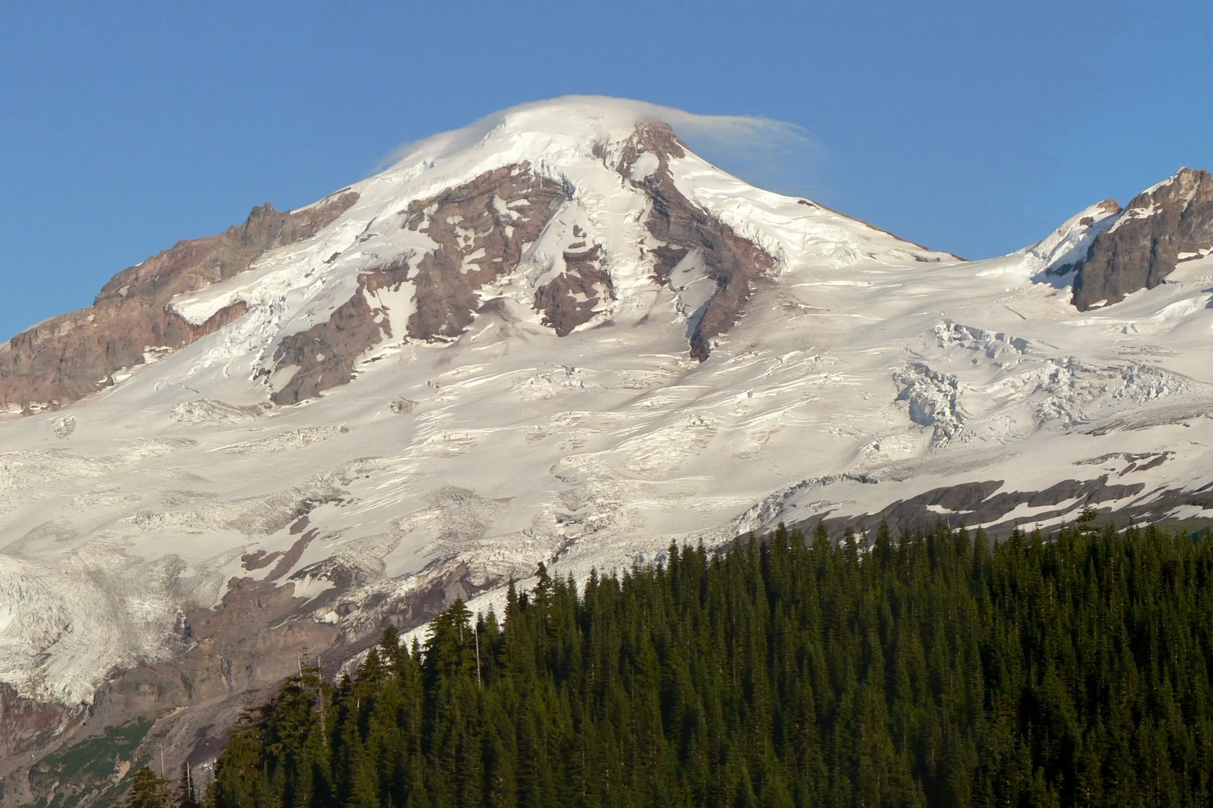 Glaciated summit of Mount Baker with Grant Peak under a cloud cap above forested ridges in Whatcom County