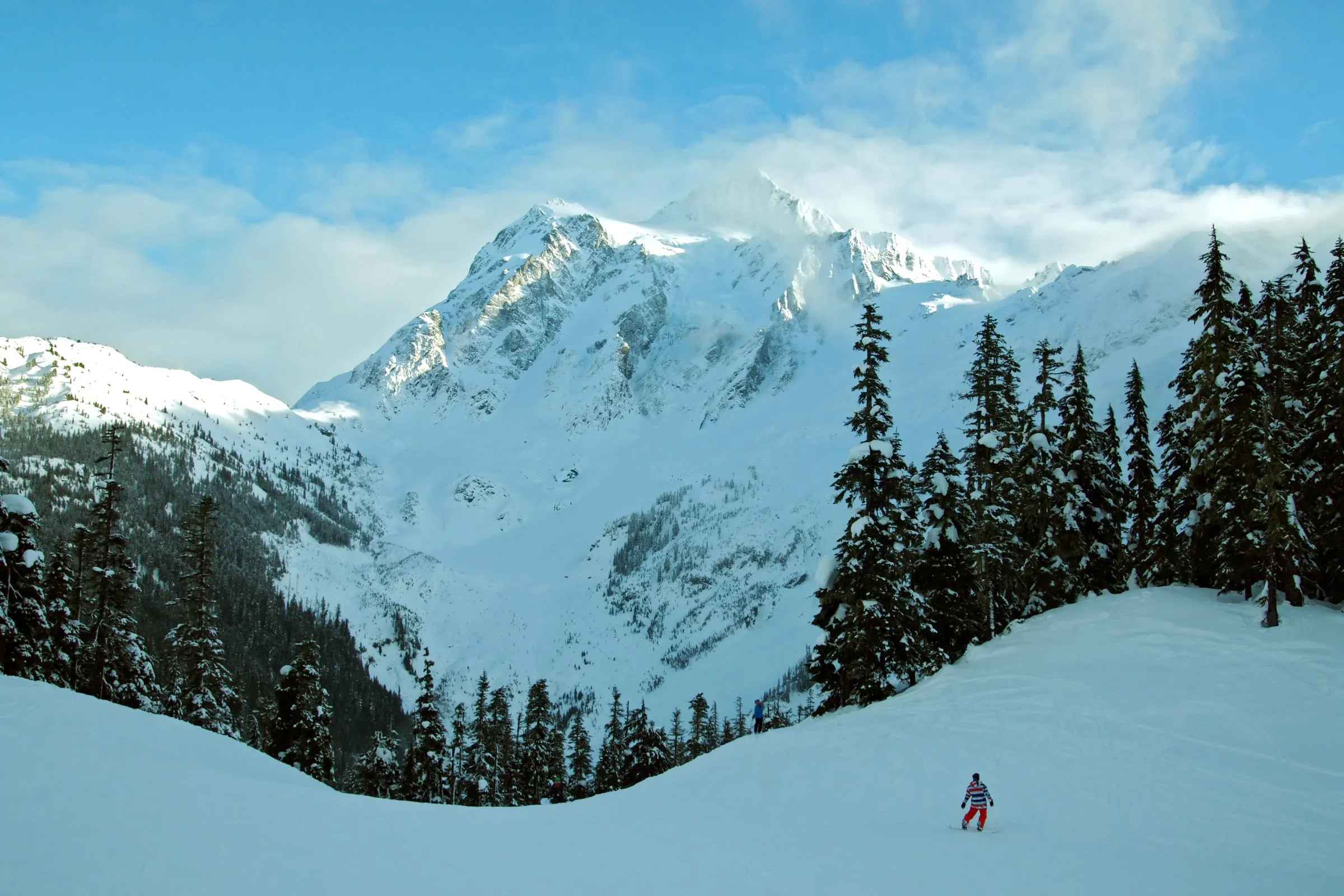 Lone snowboarder on a groomed run at Mt. Baker Ski Area with Mount Shuksan rising behind