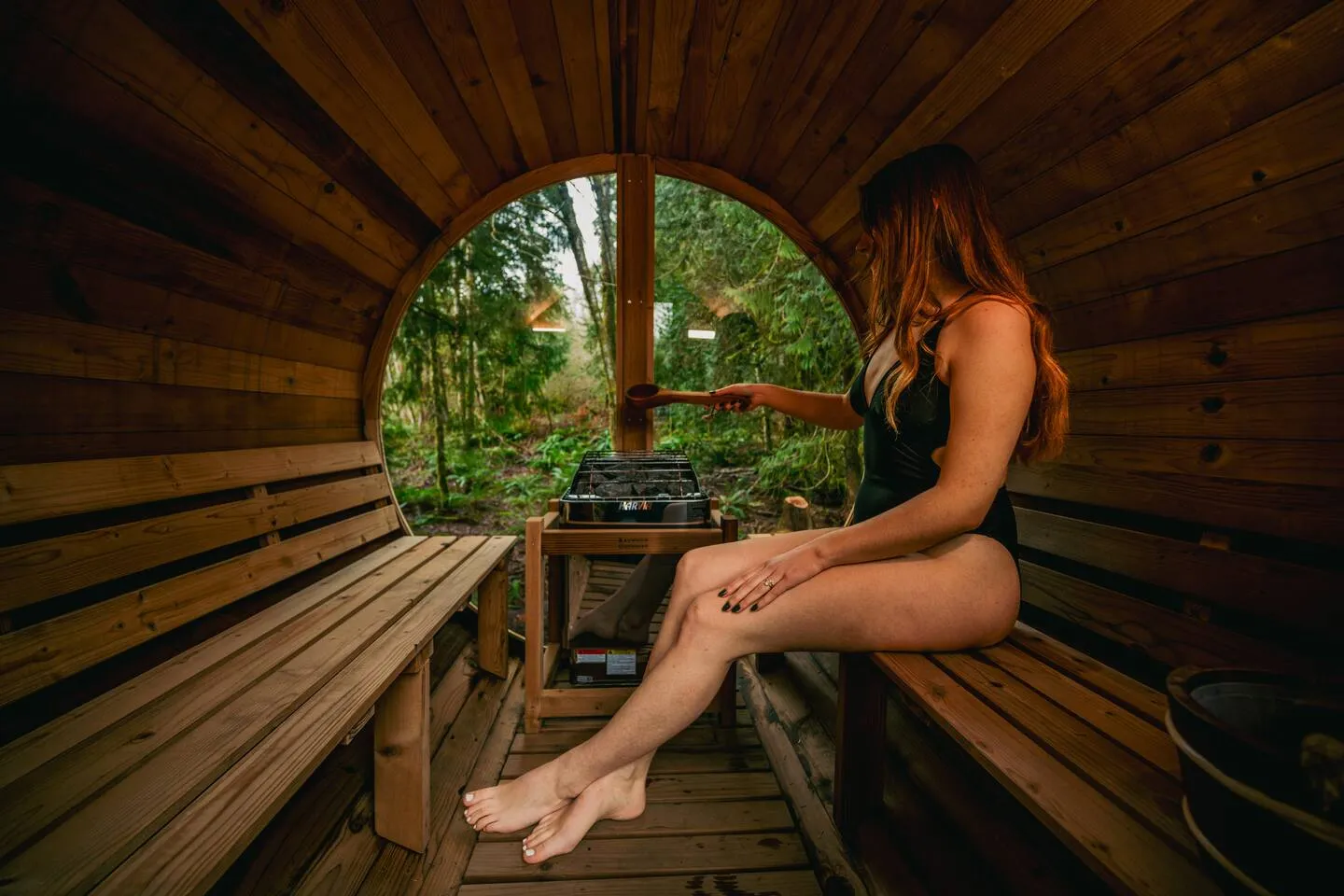 Guest relaxing inside the cedar barrel sauna with a round forest-view window
