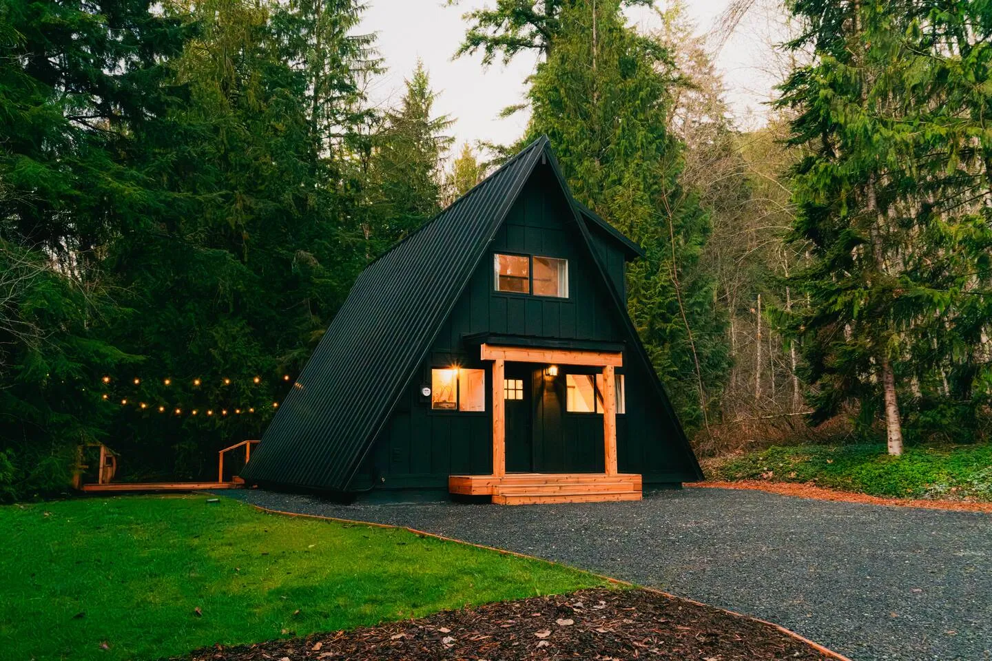 The black A-frame cabin on its green forest lawn