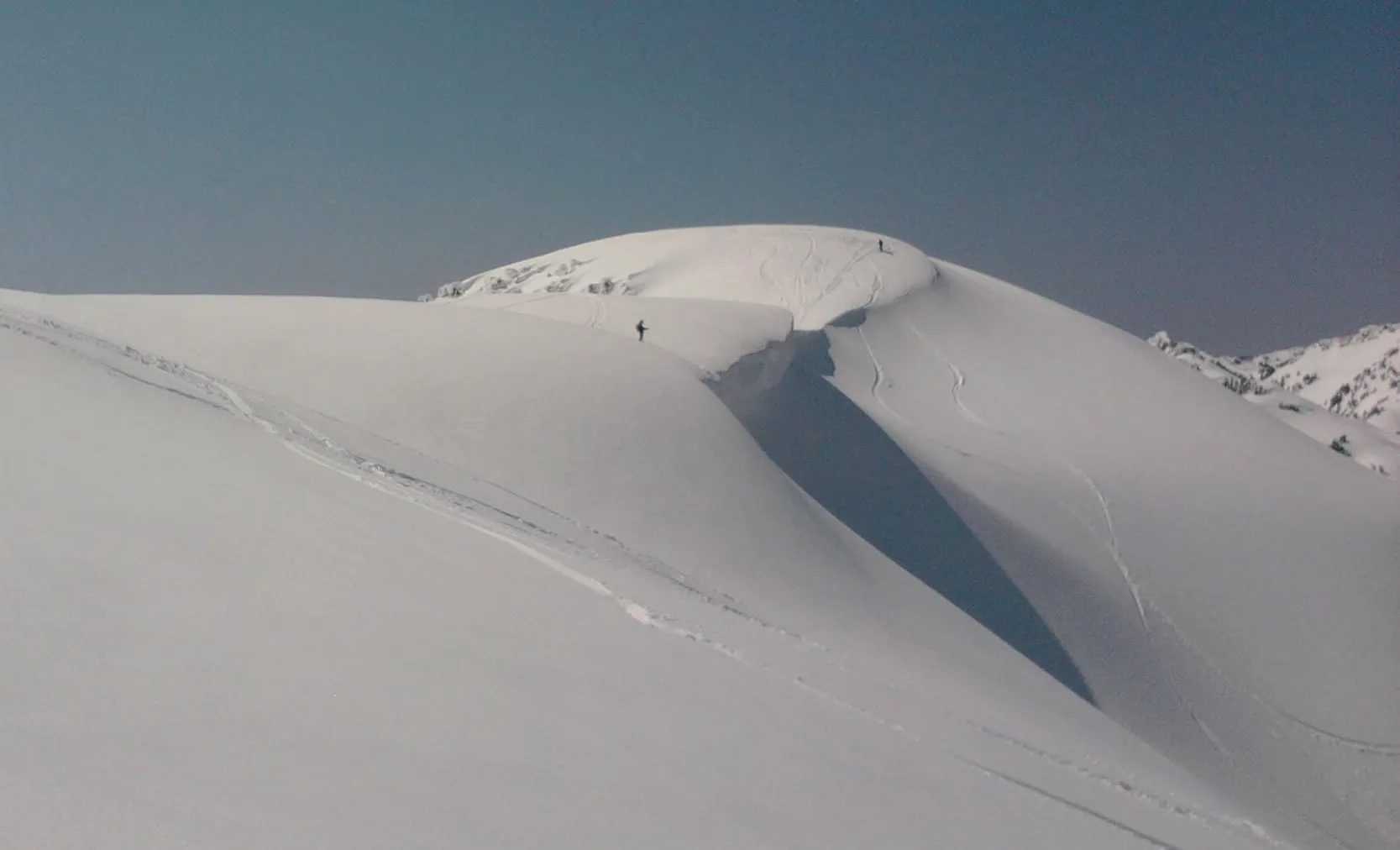 A long wind-formed cornice along the Shuksan Arm ridge above Mt. Baker Ski Area, with ski tracks on the loaded slope below it