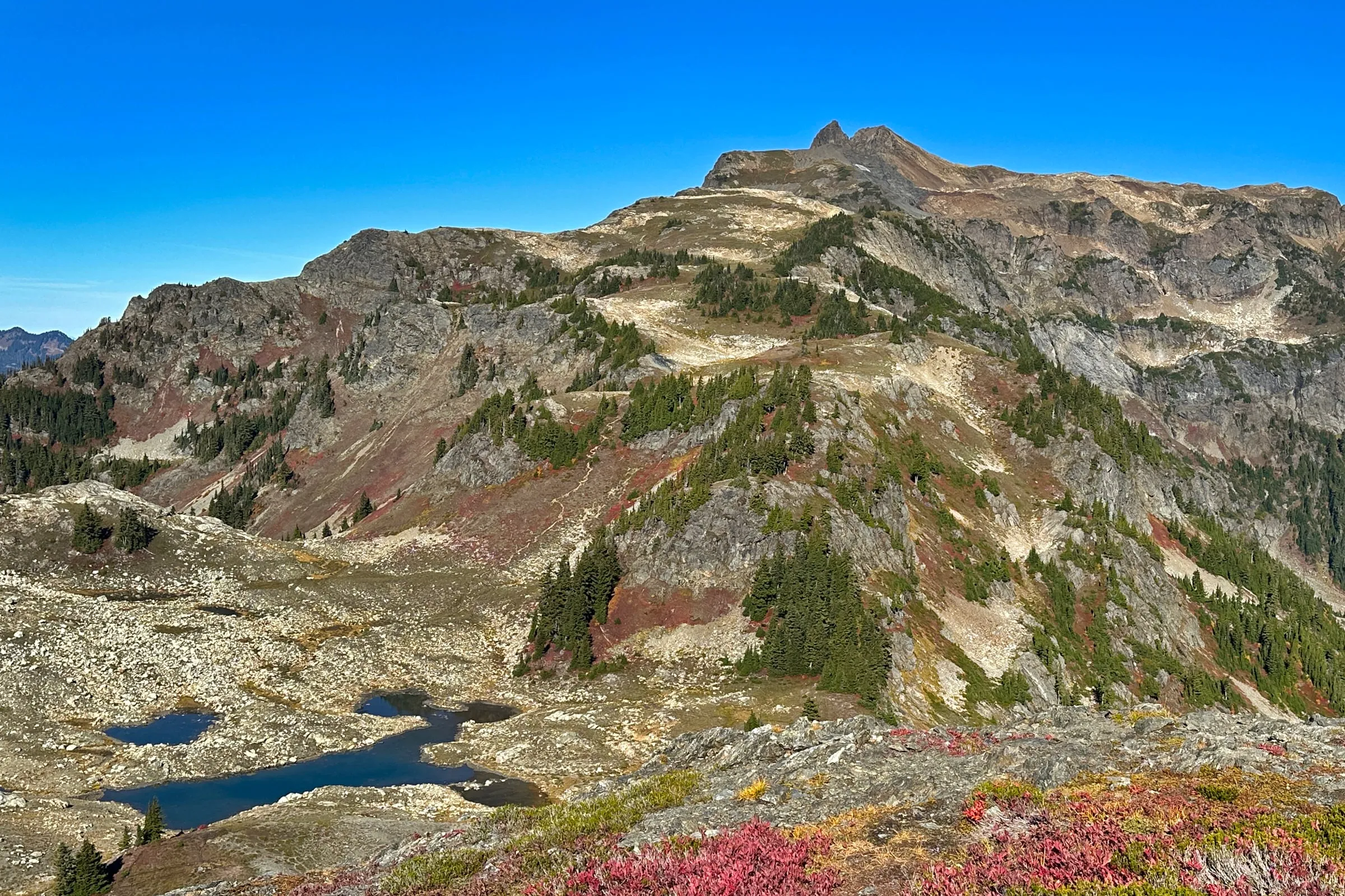 The Yellow Aster Butte summit block above an alpine tarn with the trail visible across the slope